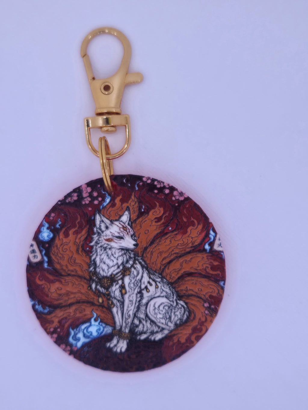 Round nine-tailed fox keychain with raised artwork clipped to a gray bag